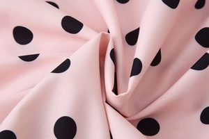 Close-up detail of soft pink chiffon fabric featuring bold black polka dot pattern