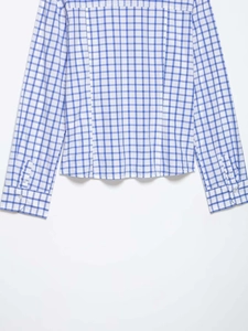 Détail de chemise à carreaux bleu et blanc montrant le poignet boutonné et le tissu