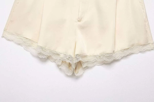 Detail of beige satin shorts featuring delicate scalloped lace trim and waist button decor