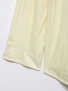 Detail view of a pale yellow poplin shirt cuff featuring a white button and fine stitching