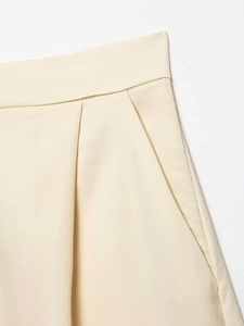 Detail view of beige satin shorts showing high-waist pleats and smooth fabric texture