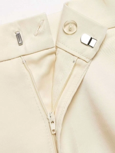 Detail of waist closure featuring a clear button, metal hook, and zipper on beige trousers