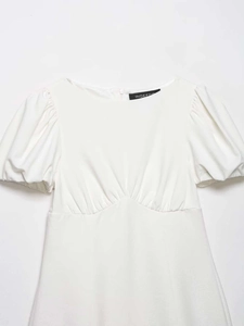 Detail of white dress with puff sleeves, pleated texture, and hidden back zipper