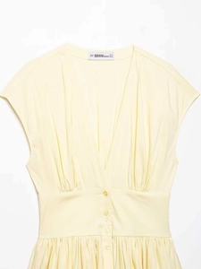 Detail of light yellow V-neck dress featuring waist pleats and matching round buttons