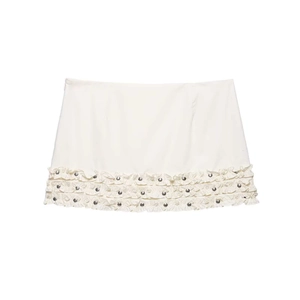 Close-up of white mini skirt detail with layered ruffles and silver metal studs