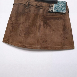Flat lay of a brown suede mini skirt featuring a decorative patch and waist belt loops
