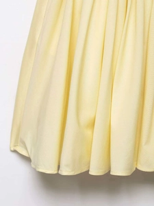 Close-up of light yellow pleated dress fabric showing fine texture and hem stitching