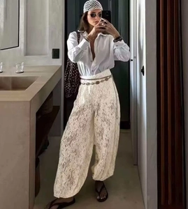 Detail of white lace wide-leg trousers featuring intricate crochet patterns and loose fit