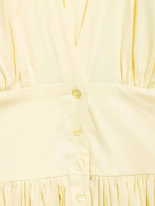 Detail of V-neckline with resin buttons and pleated waist on a yellow sleeveless dress