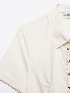 Close-up of ruffled placket and silver buttons on a cream short-sleeve shirt