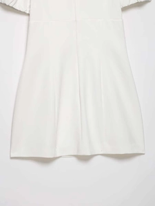 Detailed close-up of white A-line dress hem featuring pleated woven fabric and clean seams