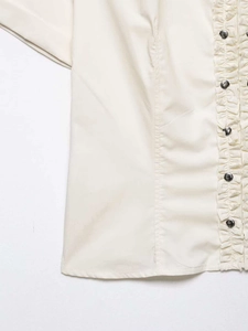 Detail of cream short-sleeve shirt with metallic buttons and ruffled pleated placket