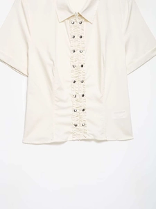 Detail of cream short sleeve shirt featuring ruffled placket and metallic rivet accents