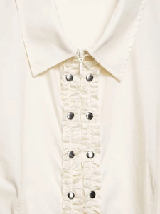 Detail of cream blouse featuring ruffle trim, metal snaps, and hidden zipper closure