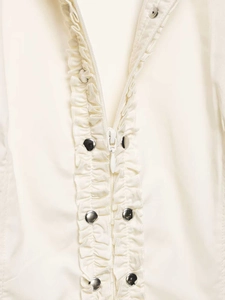 Detail of ruffled trim and silver snap buttons on a cream summer shirt with hidden zipper