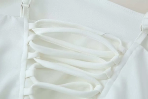 Close-up of white summer dress featuring criss-cross lace-up details and pleated texture