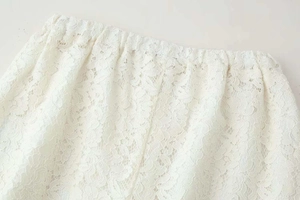 Detailed close-up of white lace trousers featuring floral patterns and elastic waistband