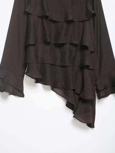 Detailed view of layered asymmetrical ruffles on black chiffon blouse with flared cuffs