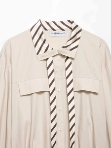 Close-up of beige shirt featuring striped satin ribbon collar and front pocket details