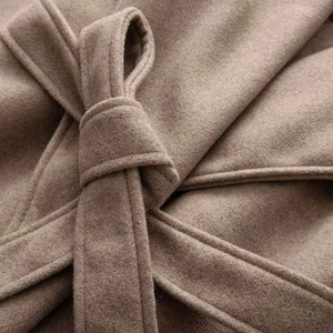 Detailed macro shot of dark camel wool coat fabric with waist tie and soft texture