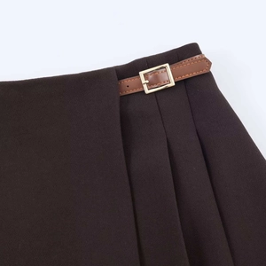Détail d'une jupe plissée chocolat avec une ceinture en cuir marron et boucle dorée