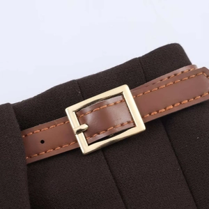 Detail d'une jupe plissee marron fonce avec ceinture assortie en simili cuir et boucle dorée