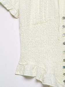 Detail of smocked waist with pearl buttons on beige seersucker ruffled shirt
