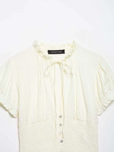 Detail of light yellow smocked blouse with ruffle collar and bow tie neckline texture