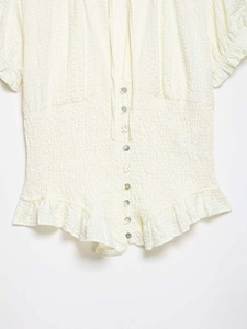 Detail of light beige seersucker shirt with smocked waist and delicate ruffle hemline