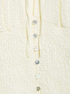 Detail of light yellow seersucker fabric featuring shell buttons and a tie-up drawstring