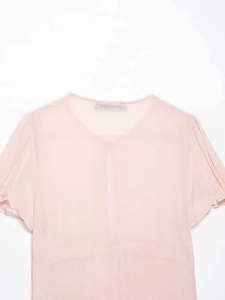 Detail of light pink chiffon top featuring ruffled short sleeves and a round neckline