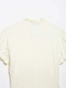 Detail of light yellow smocked waist top with seersucker texture and ruffled bubble sleeves