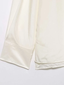 Detail of silk-satin cream blouse showing smooth stitching and side slit hem design