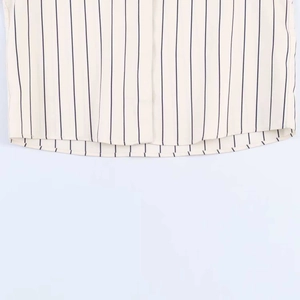 Close-up of hem stitching on loose striped shirt featuring fine vertical navy blue stripes