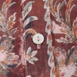Détail macro du tissu à imprimé floral vintage avec un bouton crème sur la chemise