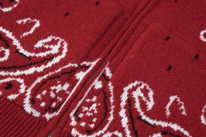 Gros plan du cardigan en maille rouge avec motif paisley et détail de fermeture éclair