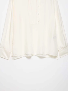 Detail view of smooth ivory satin fabric and buttoned cuff on long-sleeve shirt