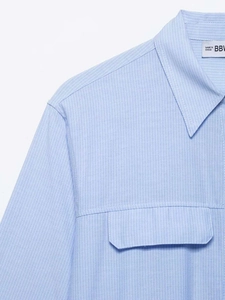 Detail of light blue striped cotton shirt featuring chest flap pocket and branded woven label