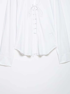 Detail of white long sleeve shirt showing lace-up front with metal eyelets and curved hem