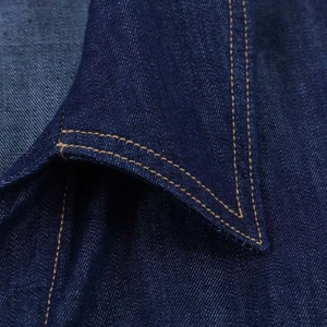 Détail du col d'une chemise en jean bleu foncé avec des doubles surpiqûres jaunes