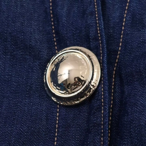 Gros plan de boutons dorés sur une chemise en jean bleu foncé avec coutures jaunes