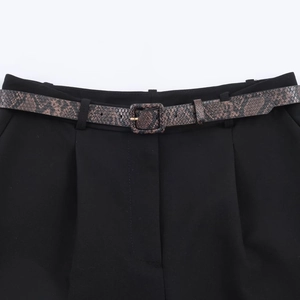 Close-up of black tailored trousers featuring an elegant snakeskin patterned belt and pleats