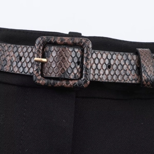 Detailed view of brown faux snake print belt with gold square metal buckle on black pants