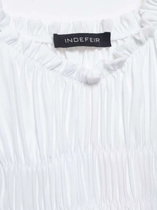Detailed view of the ruffled neckline and smocked design on a white pleated blouse