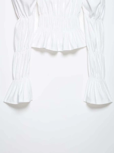 Close-up of smocked waist detail and ruffle bell sleeves on a white blouse