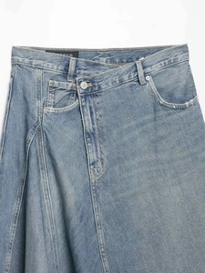 Detailed macro view of asymmetric denim waist with light blue wash and metal button