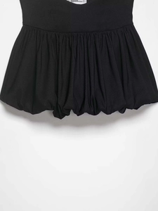 Detail view of black balloon-style hem and brand wash label on women's chic strap top