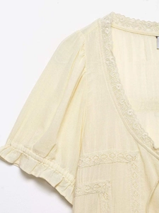 Dettaglio del top crema con scollo a V, ricamo in pizzo bianco e maniche a sbuffo