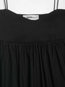 Detail of black summer camisole neck pleats with brand label and thin straps on white wall