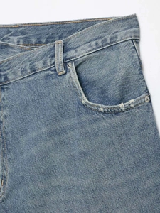 Detail of light blue washed denim skirt with asymmetric waist design and frayed pocket edges